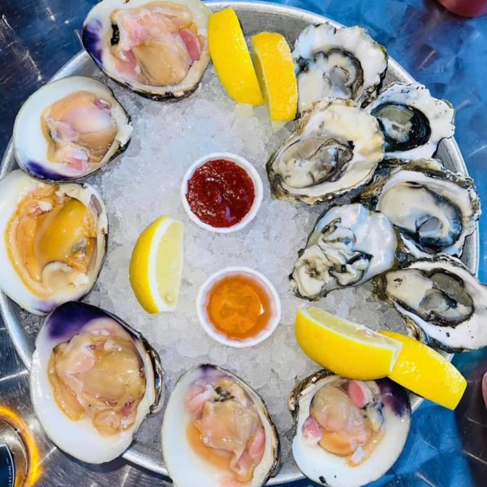 A platter of fresh Big T's oysters and clams on ice with lemon wedges and sauces.